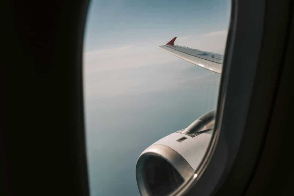View of airplane wing and engine at high altitude through a passenger window during a daytime flight.